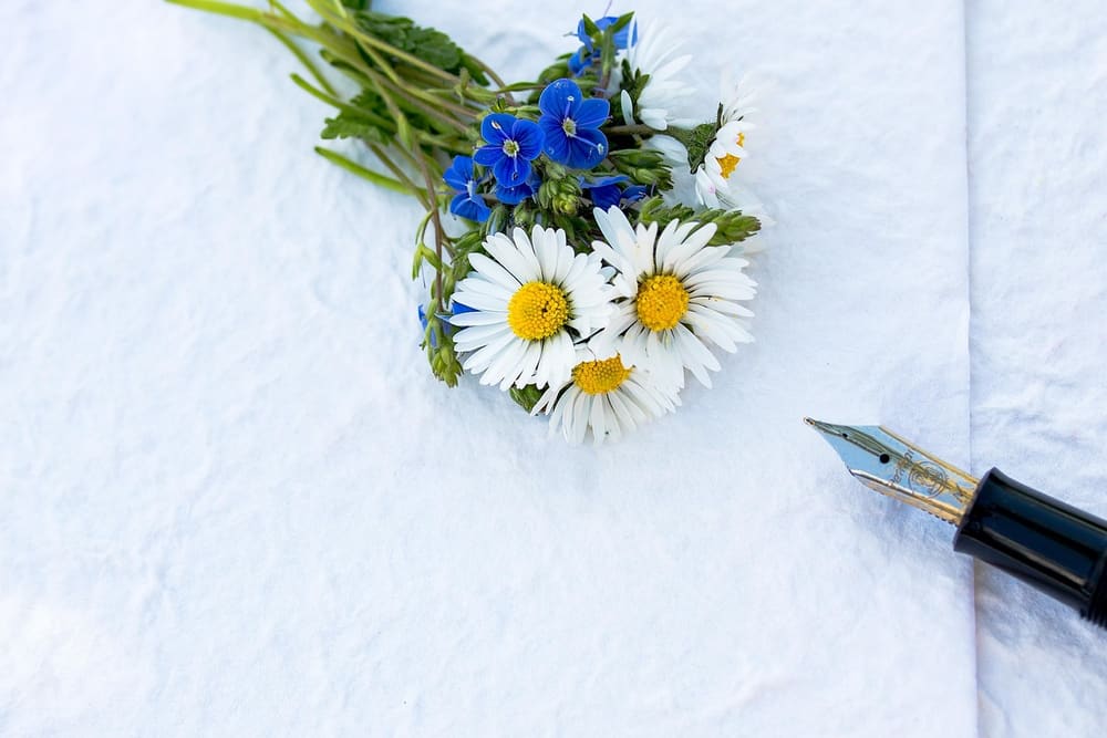 Weiße Karte mit einem kleinen Strauß Gänseblümchen und Kornblumen, daneben ein Füllfederhalter