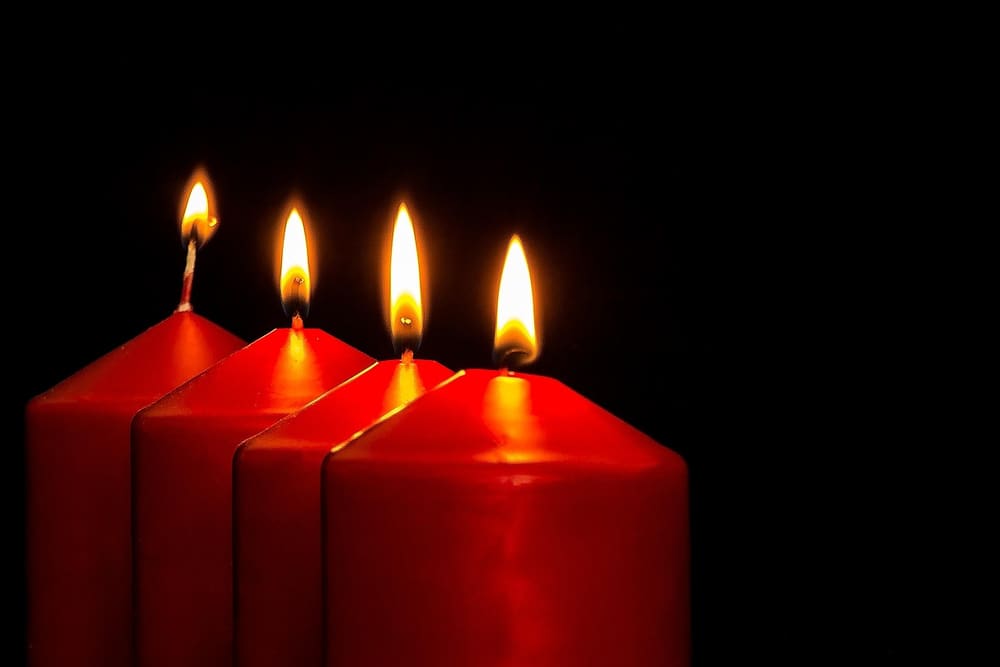 Vier brennende rote Adventskerzen vor schwarzem Hintergrund