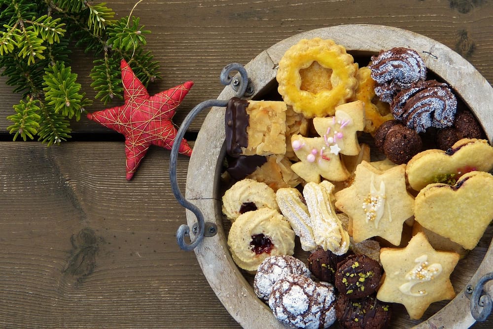 Holzschale mit verschiedenen Weihnachtsplätzchen, daneben ein roter Stern und Tannenzweige auf einem Holztisch